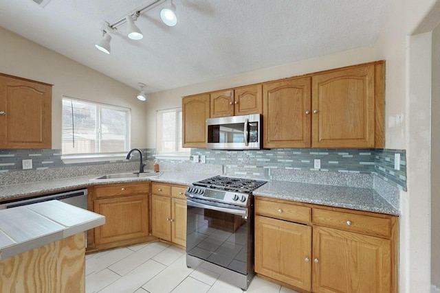 kitchen featuring light tile patterned floors, lofted ceiling, backsplash, appliances with stainless steel finishes, and a sink