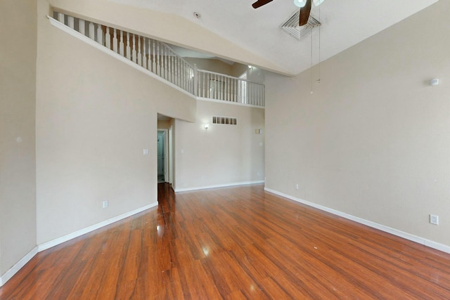 unfurnished living room featuring ceiling fan, wood finished floors, a towering ceiling, visible vents, and baseboards