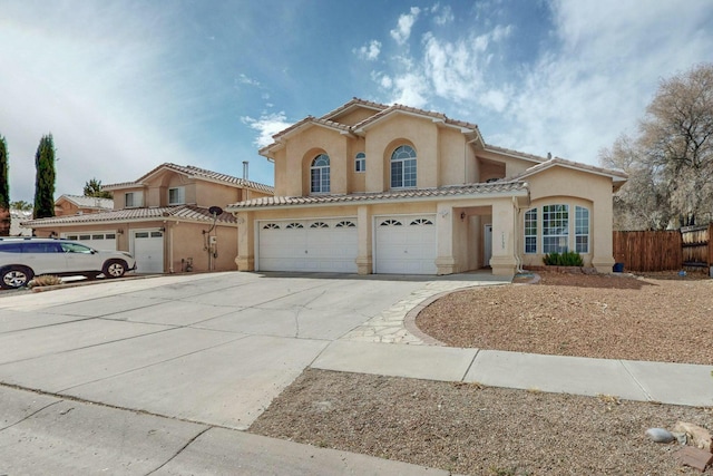 mediterranean / spanish house with a garage, fence, driveway, a tiled roof, and stucco siding