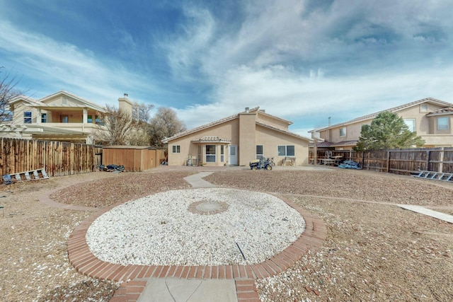 back of property with a shed, fence, an outbuilding, and stucco siding