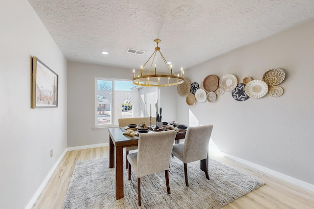 dining area featuring visible vents, a textured ceiling, wood finished floors, an inviting chandelier, and baseboards