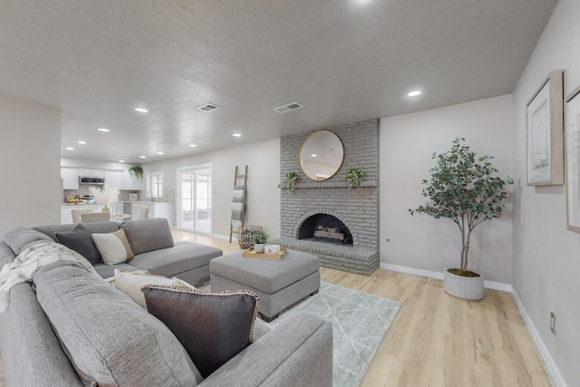 living room featuring visible vents, a textured ceiling, a fireplace, and light wood finished floors