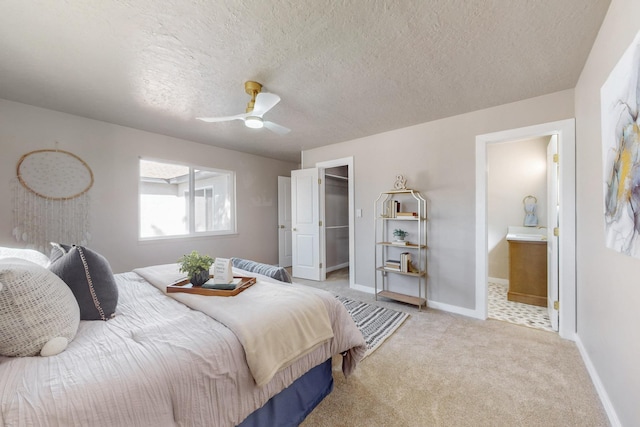 carpeted bedroom with a walk in closet, a ceiling fan, a textured ceiling, connected bathroom, and baseboards