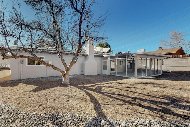 rear view of property with fence, a sunroom, and stucco siding