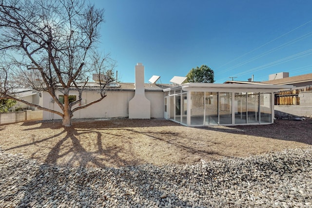 rear view of house with stucco siding, fence, and a sunroom