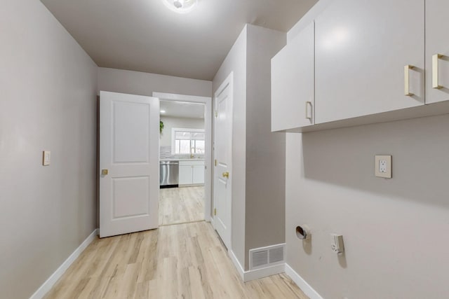 laundry area featuring visible vents, baseboards, light wood-type flooring, cabinet space, and a sink