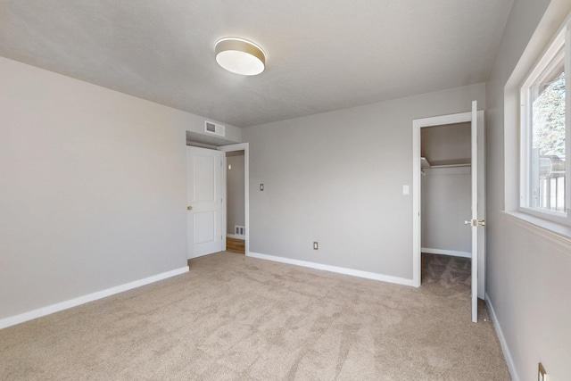 unfurnished bedroom with visible vents, a walk in closet, a closet, carpet, and baseboards