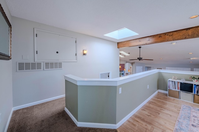 hallway featuring light wood finished floors, visible vents, baseboards, lofted ceiling with skylight, and an upstairs landing