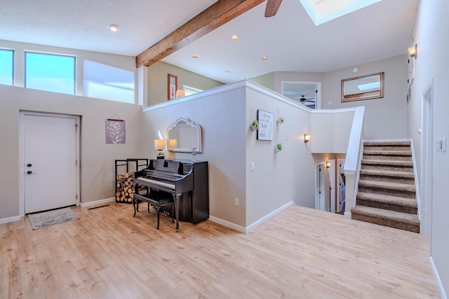 entryway featuring ceiling fan, wood finished floors, baseboards, stairway, and lofted ceiling with skylight