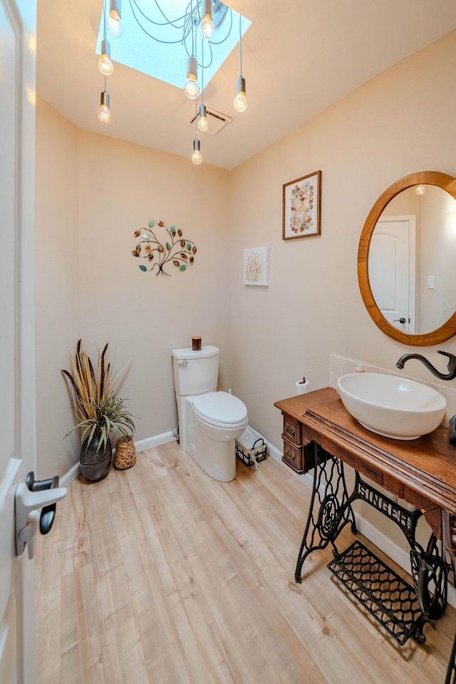 half bath featuring toilet, baseboards, a sink, and wood finished floors