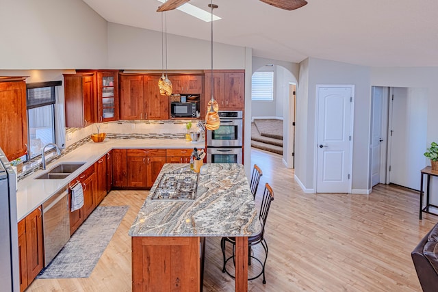 kitchen featuring arched walkways, stainless steel appliances, a sink, vaulted ceiling, and light wood-type flooring