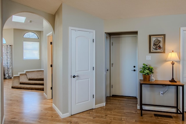 hall featuring light wood-type flooring, arched walkways, baseboards, and stairs