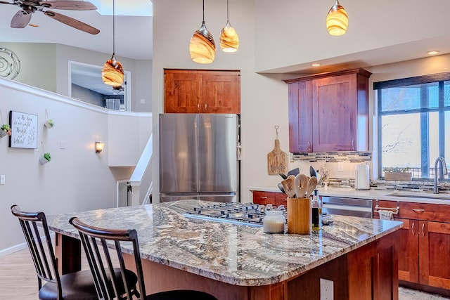 kitchen featuring light stone counters, a sink, appliances with stainless steel finishes, a center island, and pendant lighting