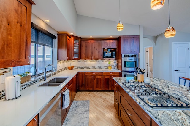 kitchen with arched walkways, a sink, vaulted ceiling, hanging light fixtures, and appliances with stainless steel finishes