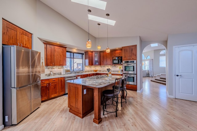 kitchen featuring a skylight, arched walkways, brown cabinetry, a breakfast bar, and stainless steel appliances