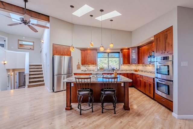 kitchen featuring a breakfast bar, brown cabinets, backsplash, appliances with stainless steel finishes, and a kitchen island