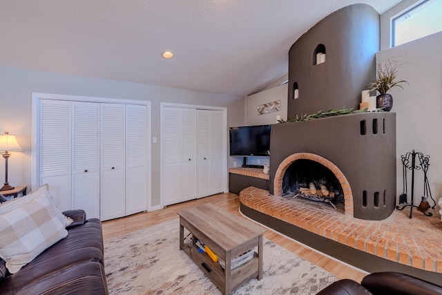 living area with lofted ceiling, a textured ceiling, a brick fireplace, and wood finished floors