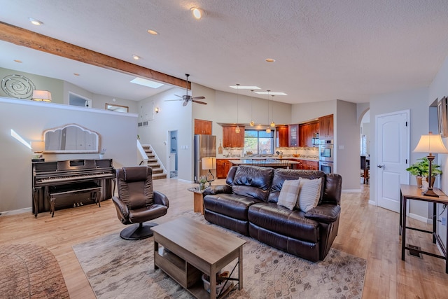 living room with light wood-style floors, arched walkways, vaulted ceiling with beams, and stairway