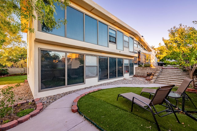 back of property with a yard, stairway, fence, and stucco siding