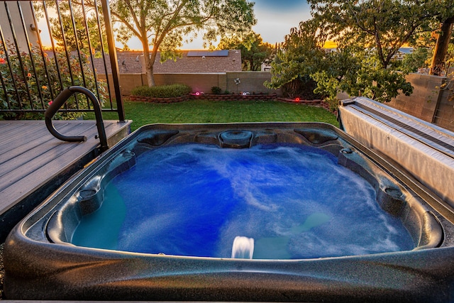 pool at dusk with a lawn and an outdoor hot tub