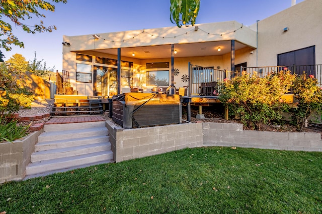 rear view of property featuring a yard, a hot tub, and stucco siding