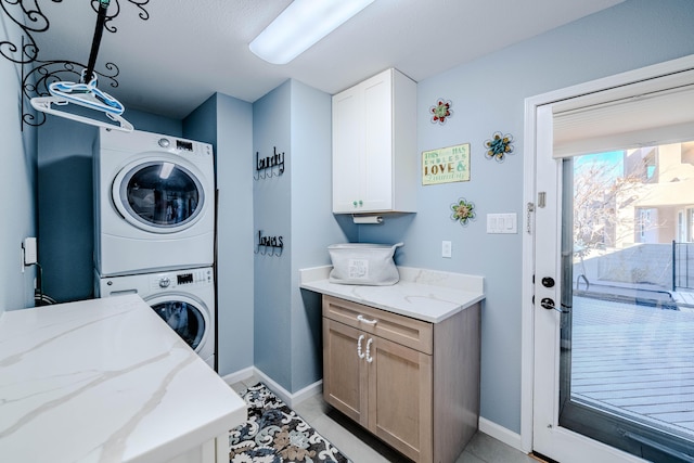 laundry area featuring stacked washer / dryer, cabinet space, and baseboards