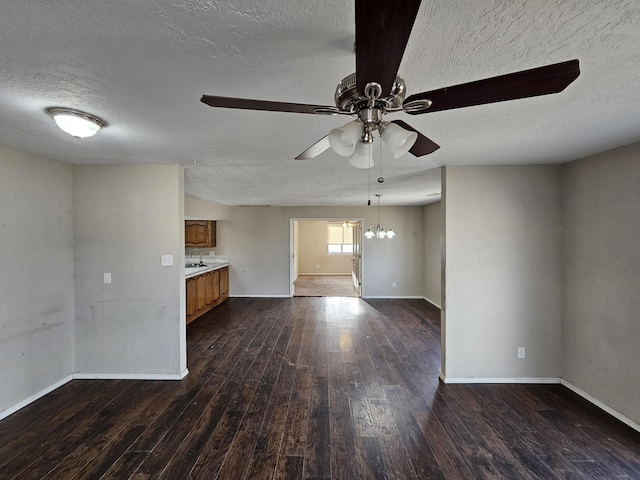 empty room featuring baseboards, dark wood-style flooring, a sink, a textured ceiling, and ceiling fan with notable chandelier