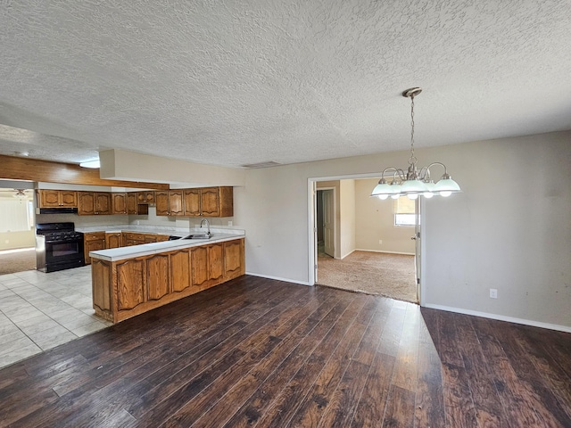 kitchen featuring brown cabinetry, light wood finished floors, a peninsula, a sink, and black gas range