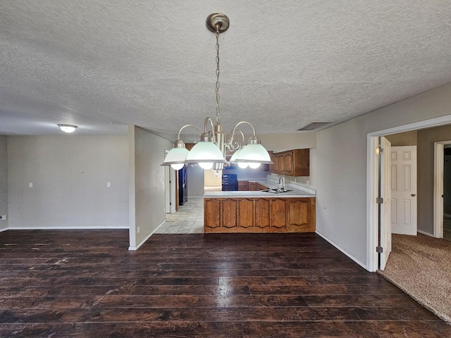 kitchen with pendant lighting, a peninsula, wood finished floors, brown cabinetry, and a sink