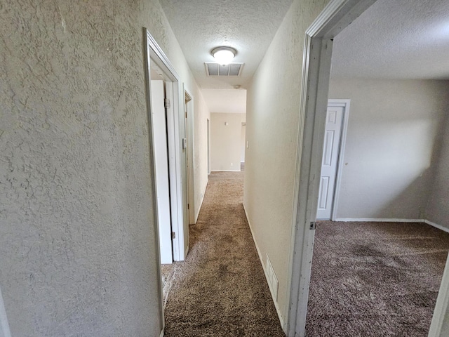 hall featuring visible vents, baseboards, carpet, a textured wall, and a textured ceiling