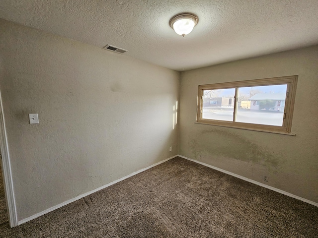 spare room with visible vents, dark carpet, baseboards, and a textured wall