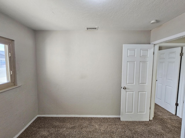 empty room featuring carpet flooring, baseboards, visible vents, and a textured ceiling