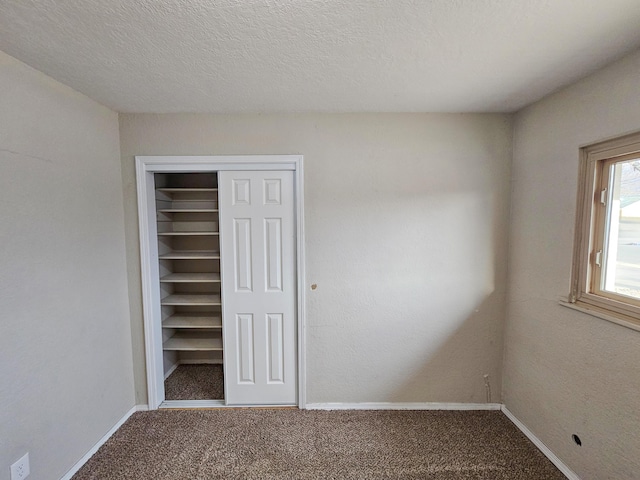 unfurnished bedroom with carpet flooring, baseboards, a closet, and a textured ceiling