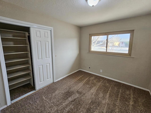 unfurnished bedroom with dark colored carpet, a closet, baseboards, and a textured ceiling