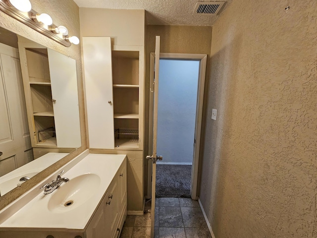 bathroom featuring vanity, baseboards, visible vents, a textured ceiling, and a textured wall