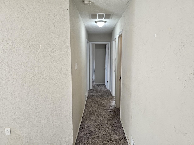 corridor featuring visible vents, a textured ceiling, dark colored carpet, and a textured wall