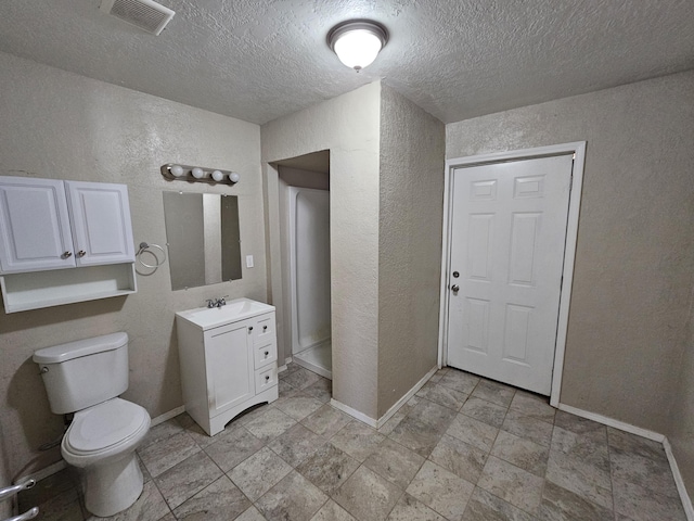 bathroom with vanity, visible vents, baseboards, toilet, and a textured wall