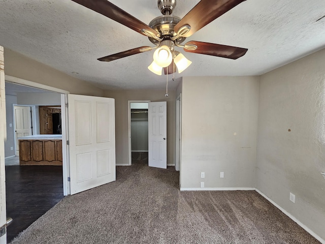 unfurnished bedroom featuring a walk in closet, baseboards, ceiling fan, carpet, and a textured ceiling