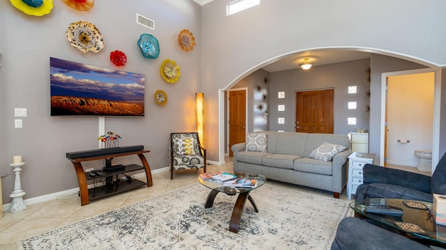 living room with arched walkways, tile patterned flooring, a towering ceiling, visible vents, and baseboards