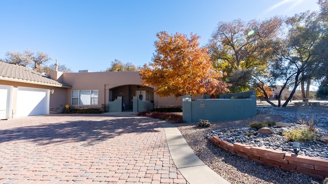 pueblo-style home with a fenced front yard, an attached garage, decorative driveway, a gate, and stucco siding