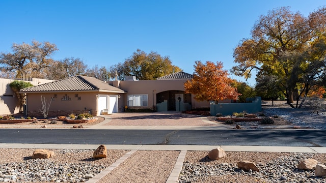 view of front of house with driveway, a fenced front yard, a tiled roof, an attached garage, and stucco siding