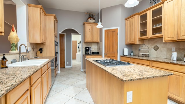 kitchen with arched walkways, stainless steel gas stovetop, a sink, and light brown cabinetry