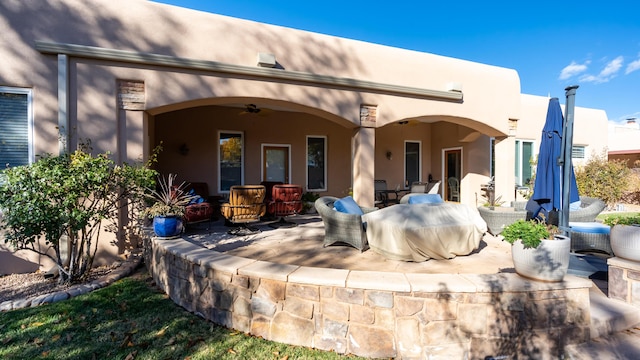 rear view of house with a ceiling fan, outdoor dining space, a patio area, and stucco siding