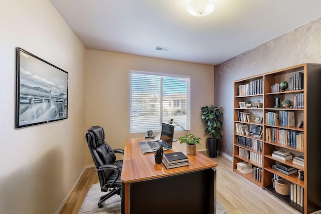 office space with light wood-type flooring, visible vents, and baseboards