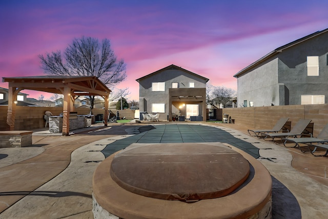 pool at dusk featuring a fenced in pool, a fenced backyard, a patio, and an outdoor kitchen