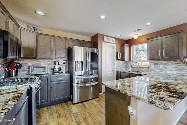 kitchen featuring light stone counters, visible vents, light wood-style flooring, appliances with stainless steel finishes, and a sink