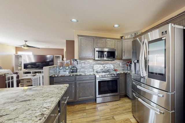 kitchen featuring open floor plan, stainless steel appliances, light stone counters, and decorative backsplash