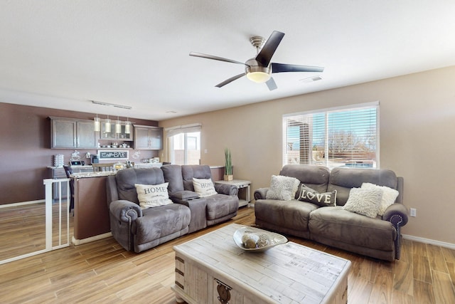 living room featuring light wood-style flooring, baseboards, and a ceiling fan