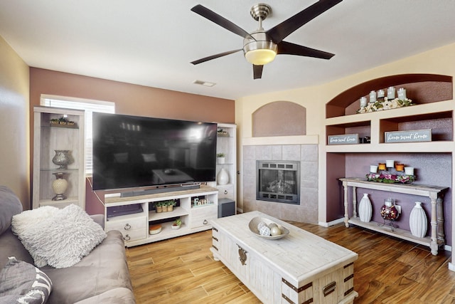 living area featuring built in shelves, a fireplace, visible vents, and wood finished floors