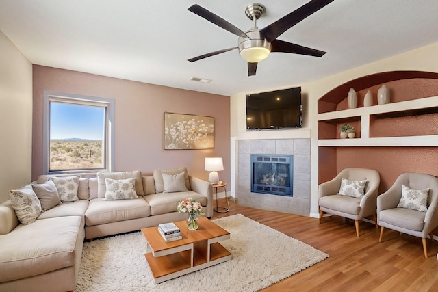 living room with built in features, visible vents, a ceiling fan, wood finished floors, and a fireplace